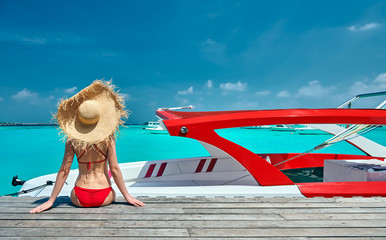 Woman in bikini sitting on jetty with boat