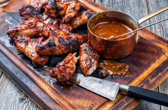 Traditional barbecue chicken wings with hot chili sauce as top view on a burnt cutting board