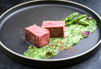 Blanched green asparagus tips with barbecue dry aged wagyu fillet steak and avocado coriander relish as closeup on a modern design plate