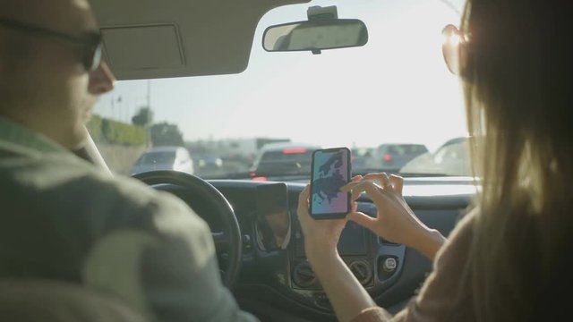 Couple using smartphone in car. Back view of man driving automobile and young woman showing map on screen. Navigation concept