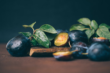 Fresh organic plums with green leaves and in drops. Whole and a half of blue plums fruit on dark vintage background. Toned image. Selective focus.