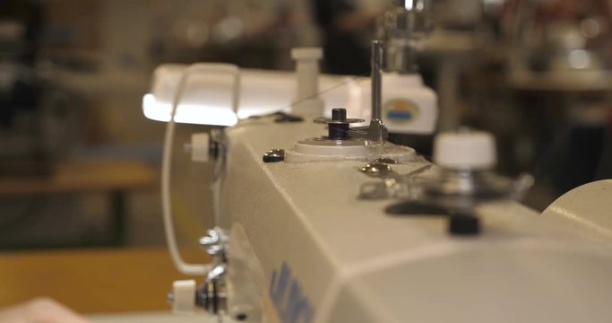 In slow motion video in a garment factory, a sewing machine embroiders various companies and engravings. Concept of: Automated work, Sewing machine, Engraving, Thread, Fabric, Needle.