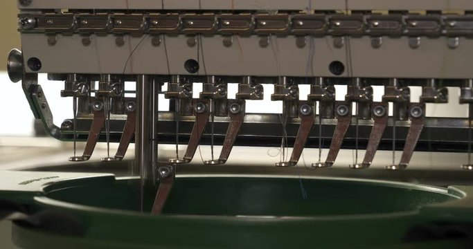 In slow motion video in a garment factory, a sewing machine embroiders various companies and engravings. Concept of: Automated work, Sewing machine, Engraving, Thread, Fabric, Needle.