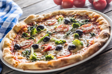 Irtalian pizza with broccoli spinach tomatoes olives and mozzarela or parmesan cheese. Mediterranean vegetarian meal