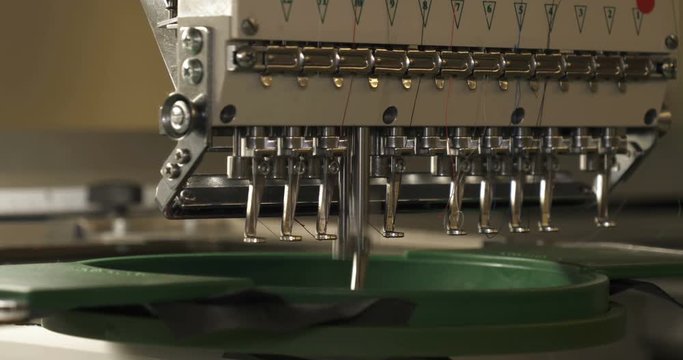 In slow motion video in a garment factory, a sewing machine embroiders various companies and engravings. Concept of: Automated work, Sewing machine, Engraving, Thread, Fabric, Needle.