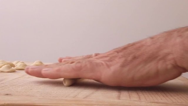Mani di uno chef stanno preparando la pasta fatta in casa su un tagliere di legno con farina di semola e integrale.