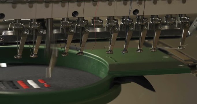 In slow motion video in a garment factory, a sewing machine embroiders various companies and engravings. Concept of: Automated work, Sewing machine, Engraving, Thread, Fabric, Needle.