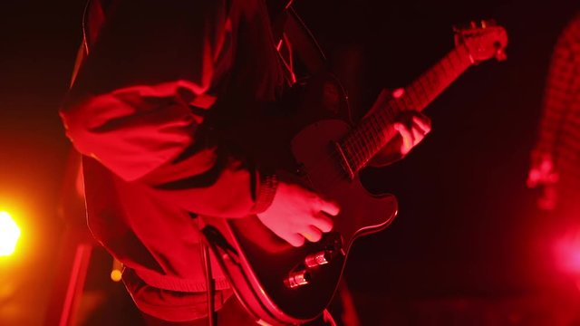 Close-up of male guitarist performing solo on stage. Cover band performance on stage in red light.