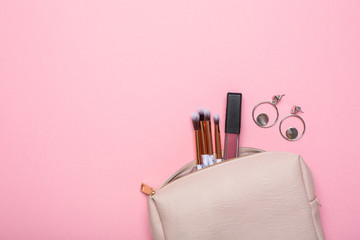 Women's cosmetic bag with makeup brushes and earrings on a pink background