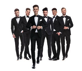 Obraz premium man buttoning his tuxedo while walking in front of team