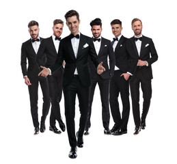  man in tuxedo walks in front of team  and welcomes