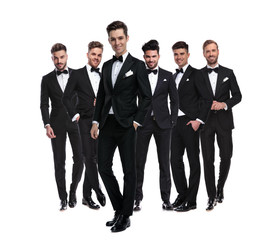 relaxed man in tuxedo standing in front of his team