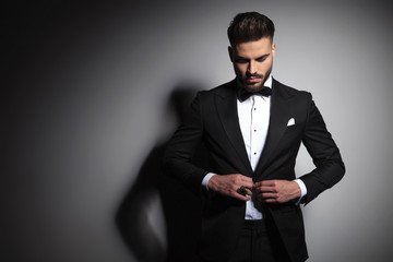 Fototapeta caucasian man in black tuxedo buttoning his suit obraz