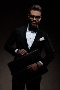 dramatic elegant man in tuxedo and sunglasses holds a suitcase