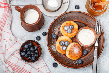 Cottage cheese pancakes, syrniki, curd fritters with fresh berry blueberry, powdered sugar, milk, honey and sour cream in a clay dish. Gourmet Breakfast. Selective focus