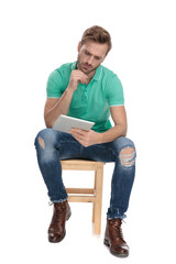 seated young guy thinking with tablet in hand