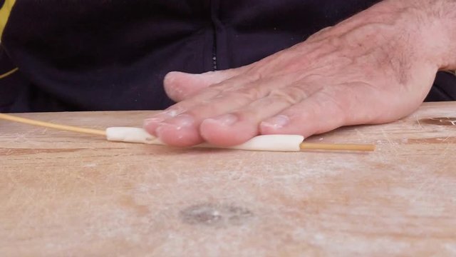 Mani di un uomo stanno stendendo la pasta filata fatta in casa su un tagliere di legno.