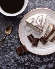 Cup of coffee and delicious jelly dessert with white & brown layers, milky glaze and pieces of dark chocolate on a spotty plate. Dessert spoon. Delicacy. Nice black background. Top view.