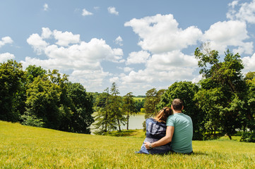 A man and woman sitting on the grass and watching summer landscape photographed from the behind