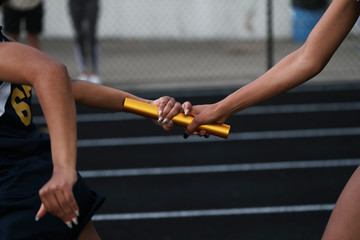 Two high school athlete exchange a baton as they particpate in a relay race