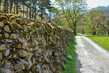 Beautiful, traditional, dry stone wall next to gravel path and green grass. Bright sunny day....