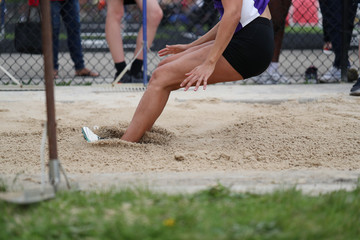 A young lady lands in the sand as she competes in the long jump, during a high school track meet. 