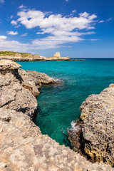 Fototapeta na wymiar Archaeological site and tourist resort of Roca Vecchia, Puglia, Salento, Italy. Turquoise sea, clear blue sky, rocks, sun, in summer. The sixteenth-century lookout tower. White clouds and strong wind.