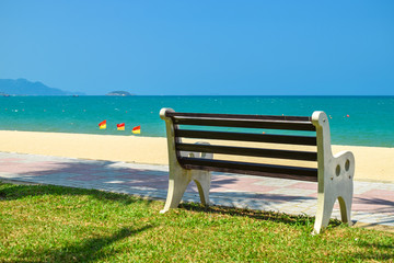 Wooden bench on beach with green lawn and flags