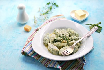 Gnocchi or dumplings with nettle or spinach on a white plate on a light blue background. Served with butter and parmesan cheese. Italian food. Selective focus
