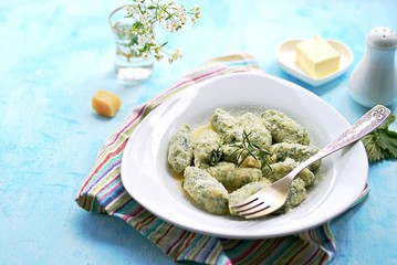 Gnocchi or dumplings with nettle or spinach on a white plate on a light blue background. Served with butter and parmesan cheese. Italian food. Selective focus