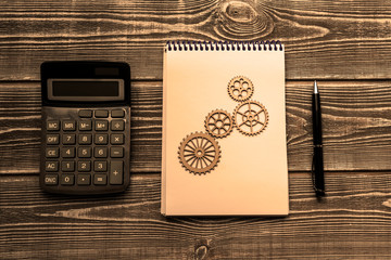 Calculator, notebook, gears, pen on a wooden background. mechanism, business ideas. planning.