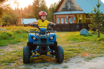 little boy 5 years children's ATV rides background village house in the summer vacation setting sun. quadbike