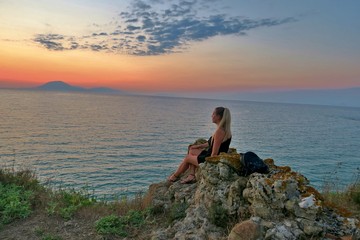 girl sits on a rock and looks at a beautiful view of the sea and sunset