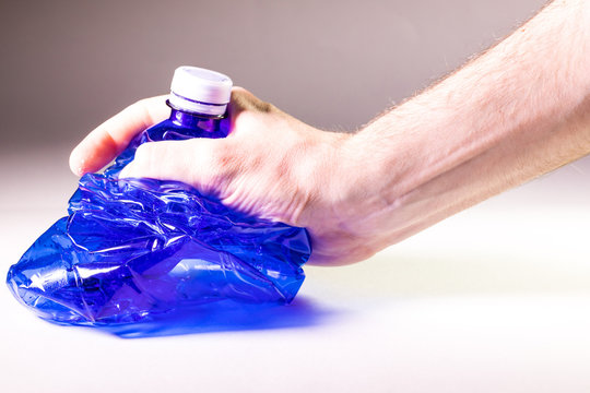 Mano che sta schiacciando una bottiglia di plastica trasparente blu per la raccolta differenziata del multimateriale. Concetto di ecologia e stop all'inquinamento.