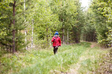 Fototapeta premium five-year-old boy in a red jacket running through the forest