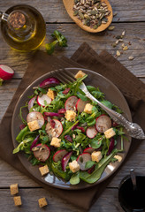 Fresh vegetable salad with radish, arugola, balsamic vinegar and croutons on dark wood