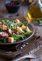 Fresh vegetable salad with radish, arugola, croutons on dark wood