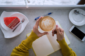 Concept of drinks and youth lifestyle, woman hands and cup of coffee. Young woman writing to do list of goals writing in diary in coffee shop. Female student taking notes in personal organizer.