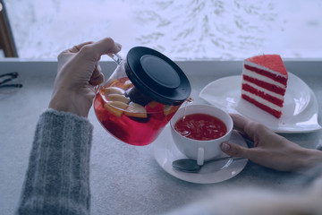 Young woman enjoying a cup of fruit tea in the coffee shop. Hot tea cup on a frosty winter window background. Cozy coffee shop atmosphere in winter. Relax concept. Warm vintage toning.