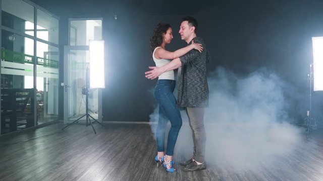 Smoke starts filling the room while a couple begin to dance in a studio. Professional dancers perform kizomba.