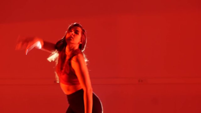 Young beautiful girl dancing modern dance on a red background in high heels, strip plastic