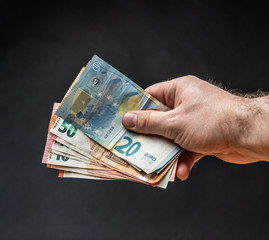 Hand holding some Euro bank notes in front of a dark background.