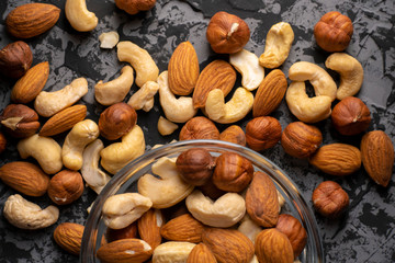 mixed different raw cocktail nuts in a bowl on a dark table, healthy and organic food concepts