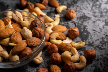 mixed different raw cocktail nuts in a bowl on a dark table, healthy and organic food concepts