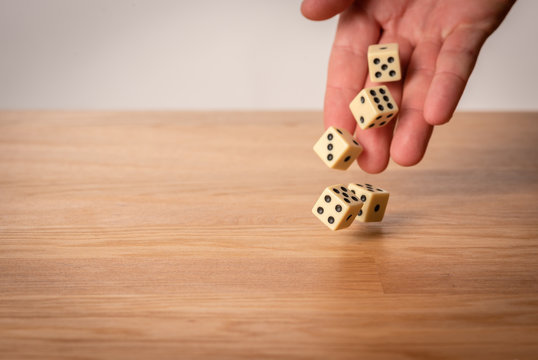 Hand throwing dice in front of a dark background.