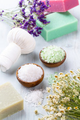 Sea salt in bowl, aroma oil in bottles, Wellness and flowers on grey textured background and flowers on vintage wooden background. Selective focus.