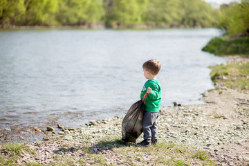 Save environment concept, a little boy collecting garbage and plastic bottles on the beach to dumped into the trash.