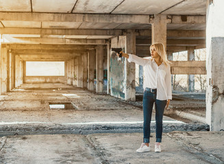 Woman in white shirt stands in an abandoned building, shoots a gun