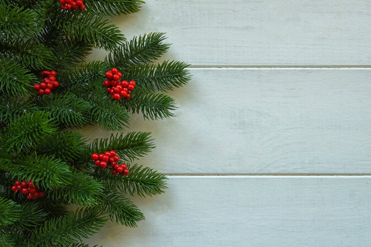 Christmas wooden background with fir branches and red berries. View with copy space.