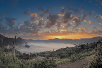sunrise at Phu Langka Photo Corner View Point, view scenic sea of fog in valley around with high mountains with yellow sun light and cloudy sky background, route 1148, Phayao, northern of Thailand.